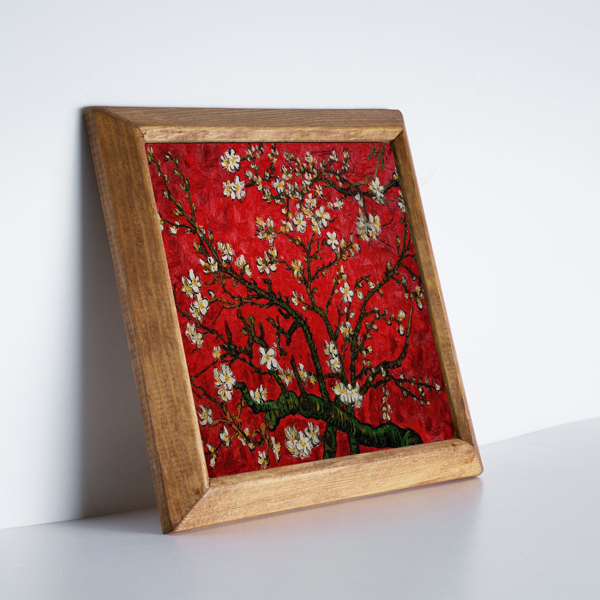 Framed artwork of a red background with floral branches on a white surface