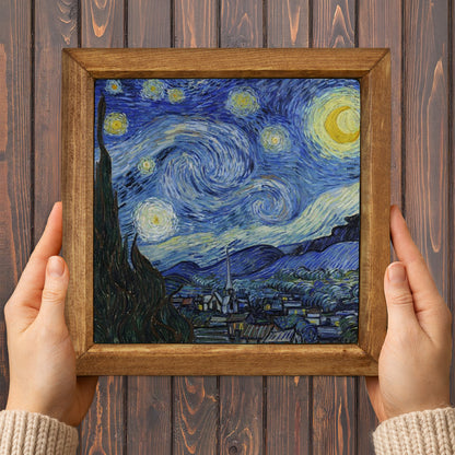 Framed artwork resembling 'Starry Night' held by hands against a wooden background