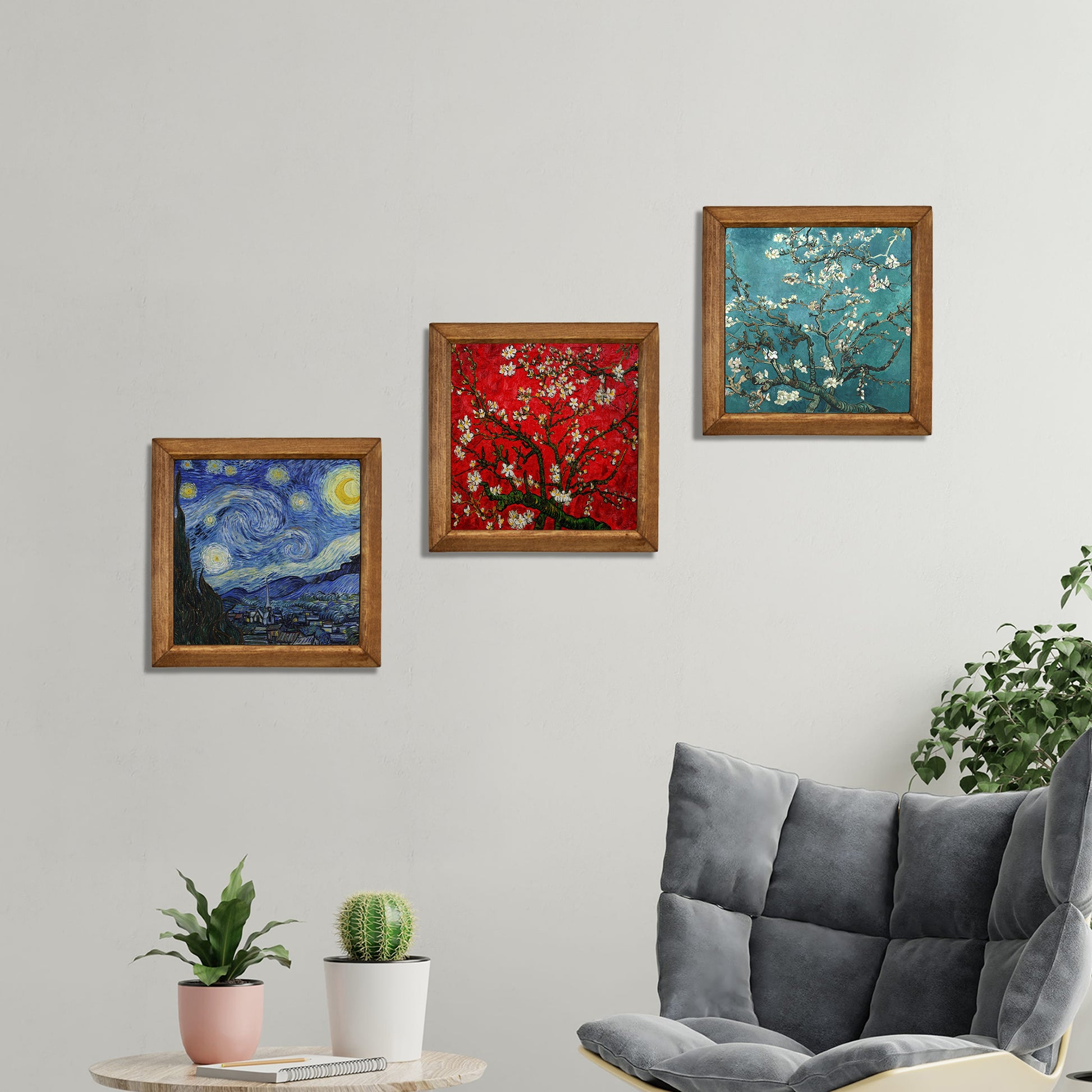 Three framed artworks on a wall above a gray sofa with plants.
