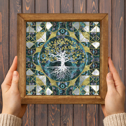 Framed artwork with a tree design held by two hands on a wooden background