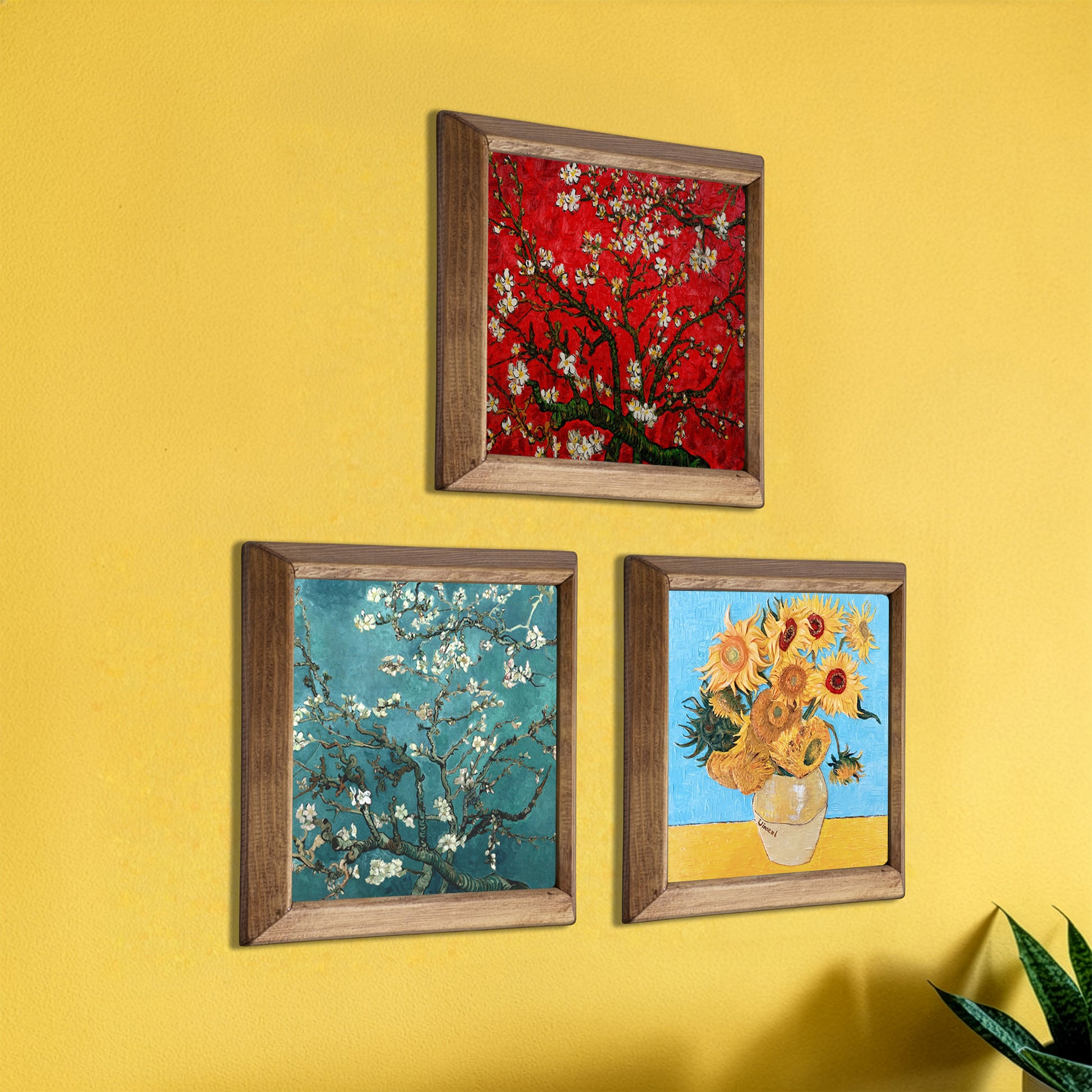 Three framed artworks on a yellow wall, including a red floral piece, a blue floral piece, and a sunflower painting.