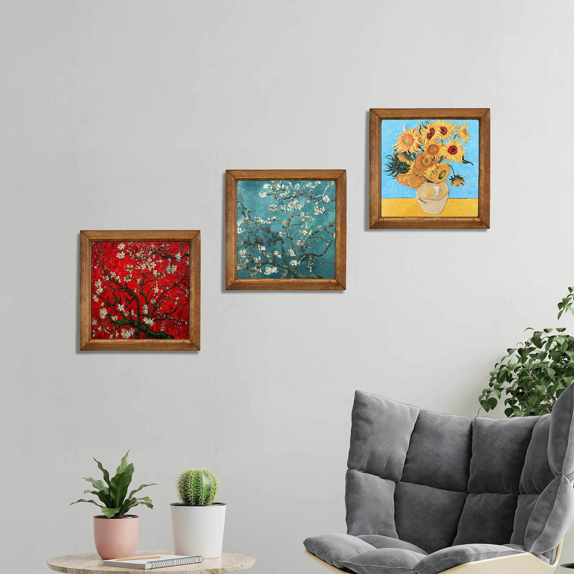 Three framed paintings on a wall above a gray sofa with plants.