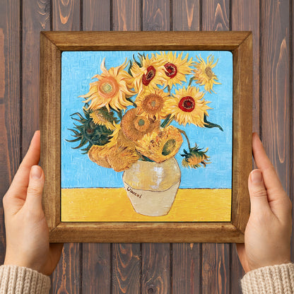 Framed artwork of Van Gogh's 'Sunflowers' held by hands on a wooden background